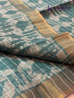 Kadamparii Silk teal semi tussar batik printed saree with abstract geometric patterns, subtle golden woven accents, soft textured fabric, tassel detailing, and elegant traditional design.