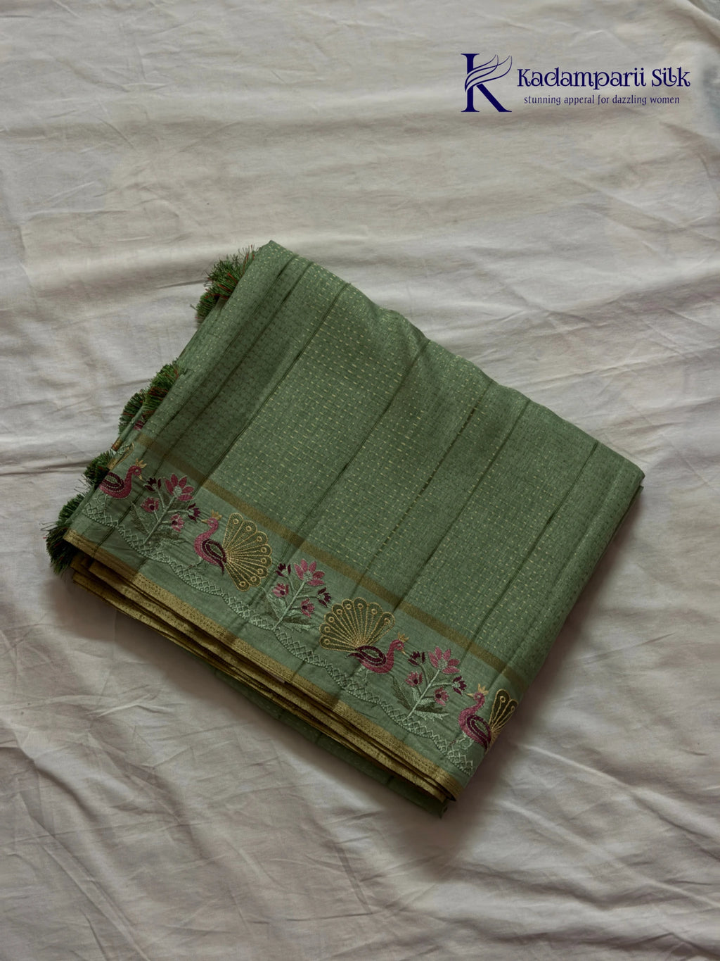 Sage green Tussar silk saree with embroidered peacock and floral border, subtle zari detailing, textured lightweight fabric, tassel finish, and elegant traditional styling by Kadamparii Silk.
