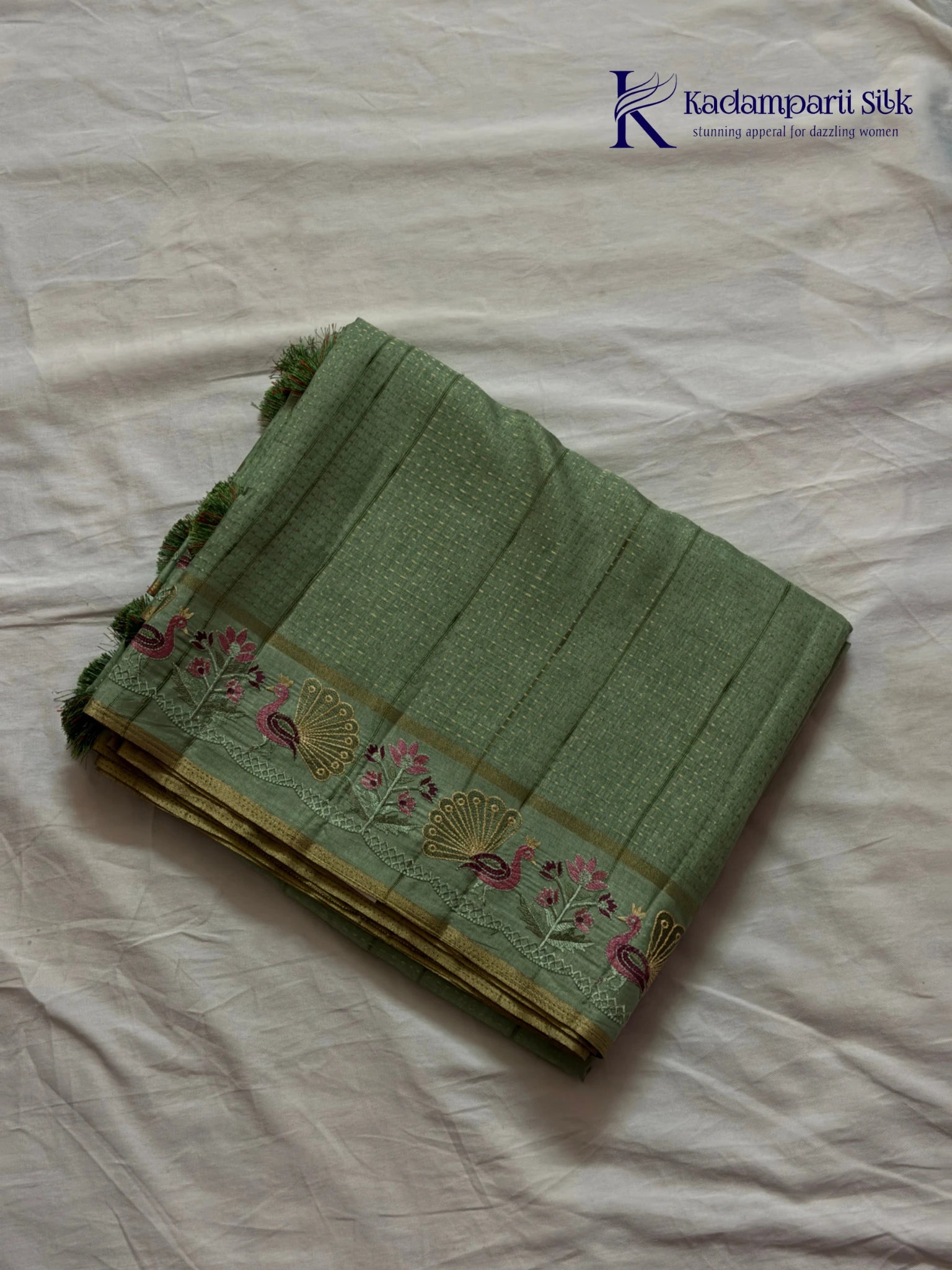Sage green Tussar silk saree with embroidered peacock and floral border, subtle zari detailing, textured lightweight fabric, tassel finish, and elegant traditional styling by Kadamparii Silk.