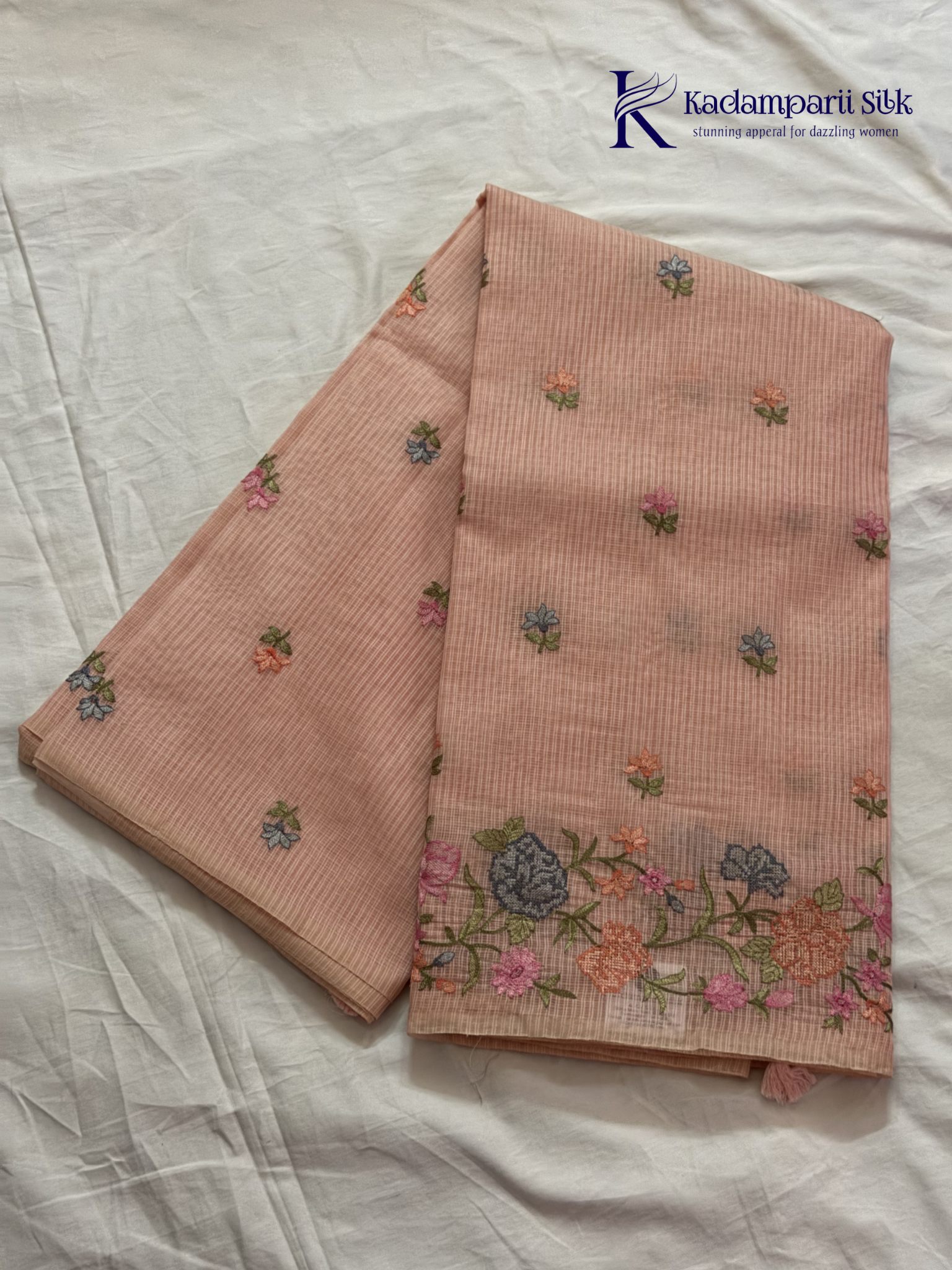 Blush pink super net saree with delicate multicolor floral embroidery, soft textured weave, lightweight sheer fabric, elegant feminine detailing, and graceful modern drape by Kadamparii Silk.