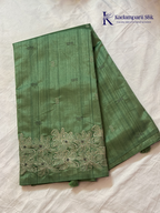 Emerald green semi raw silk saree with intricate floral embroidery, delicate embellishment detailing, rich textured finish, elegant tassels, and graceful festive drape by Kadamparii Silk.
