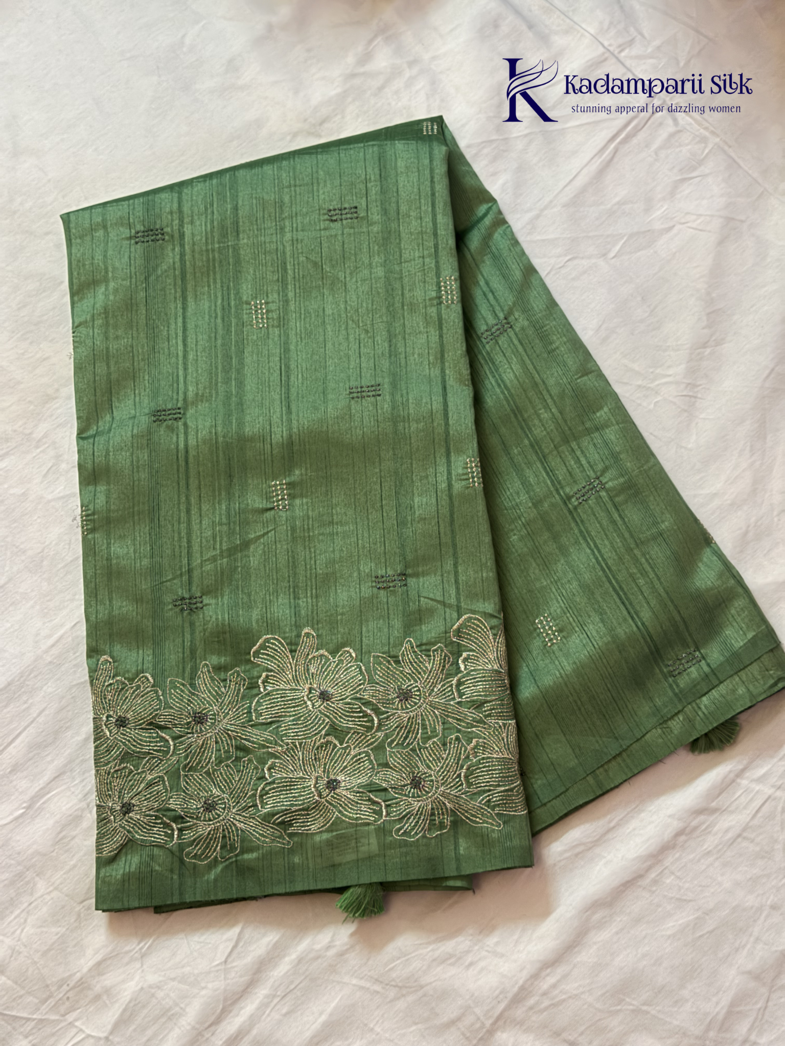 Emerald green semi raw silk saree with intricate floral embroidery, delicate embellishment detailing, rich textured finish, elegant tassels, and graceful festive drape by Kadamparii Silk.