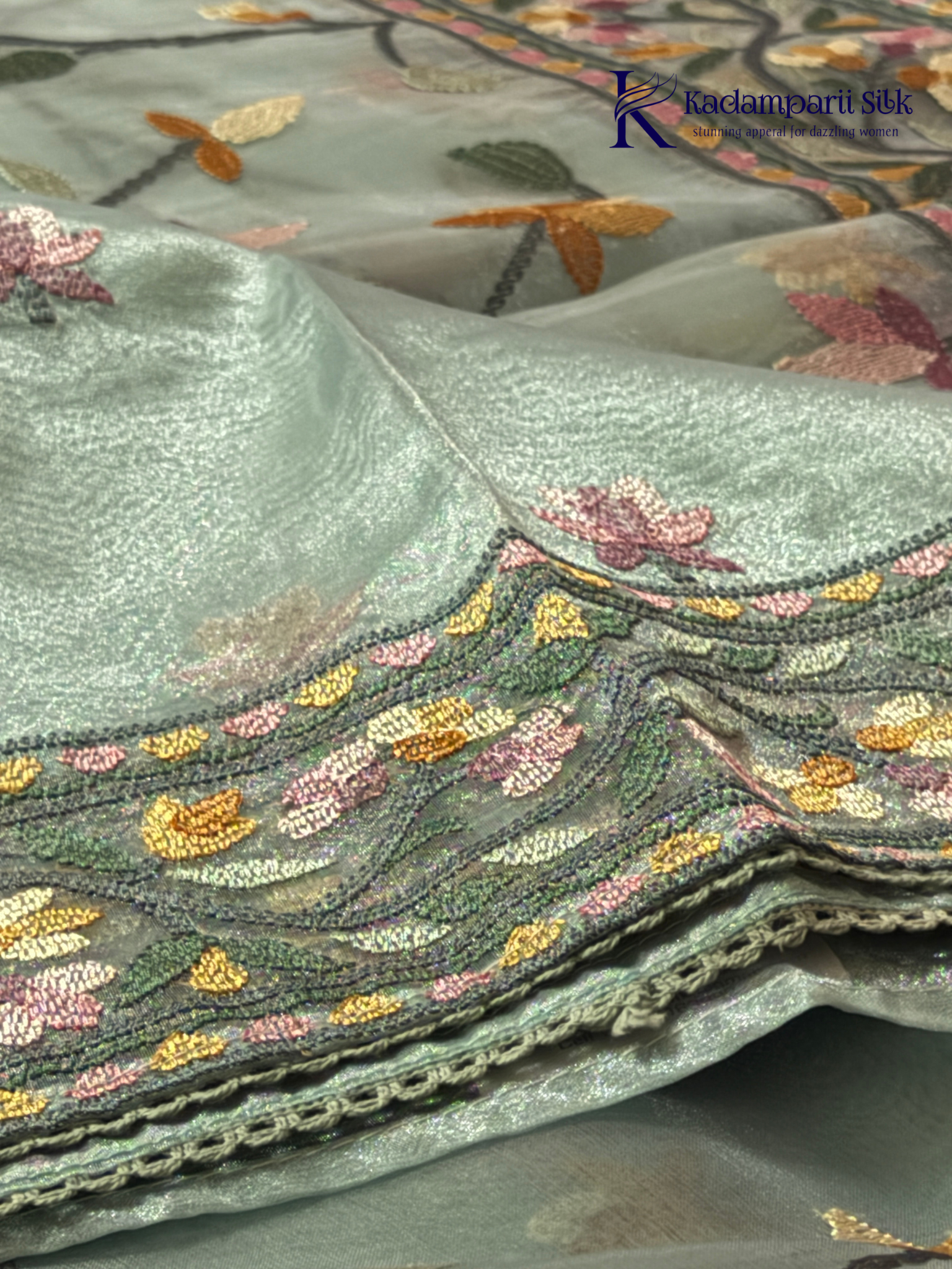 Pastel blue organza saree with multicolor floral embroidery, delicate vine patterns, embroidered border detailing, lightweight sheer fabric, and elegant festive styling by Kadamparii Silk.