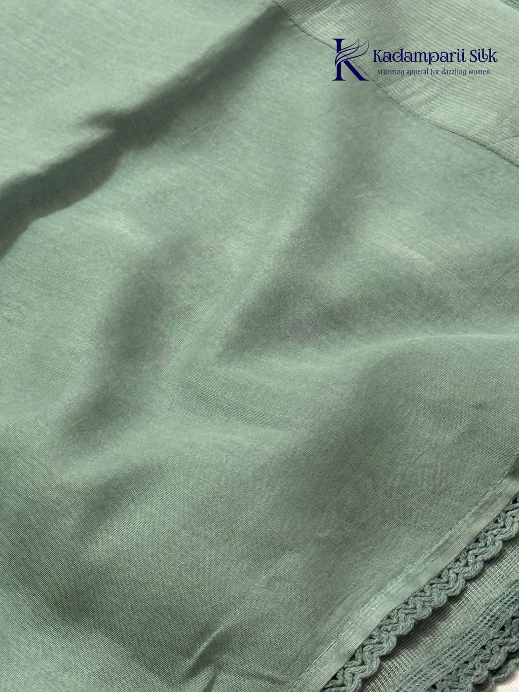 Sage green super net saree with elegant wave-pattern fancy embroidery, subtle shimmer detailing, delicate lace border, lightweight sheer texture, and graceful contemporary drape by Kadamparii Silk.
