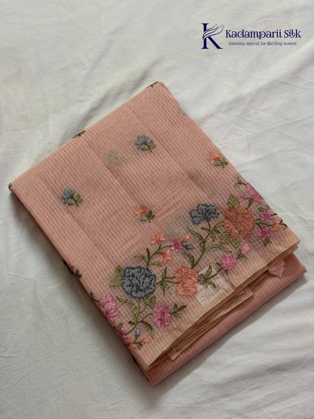 Blush pink super net saree with delicate multicolor floral embroidery, soft textured weave, lightweight sheer fabric, elegant feminine detailing, and graceful modern drape by Kadamparii Silk.
