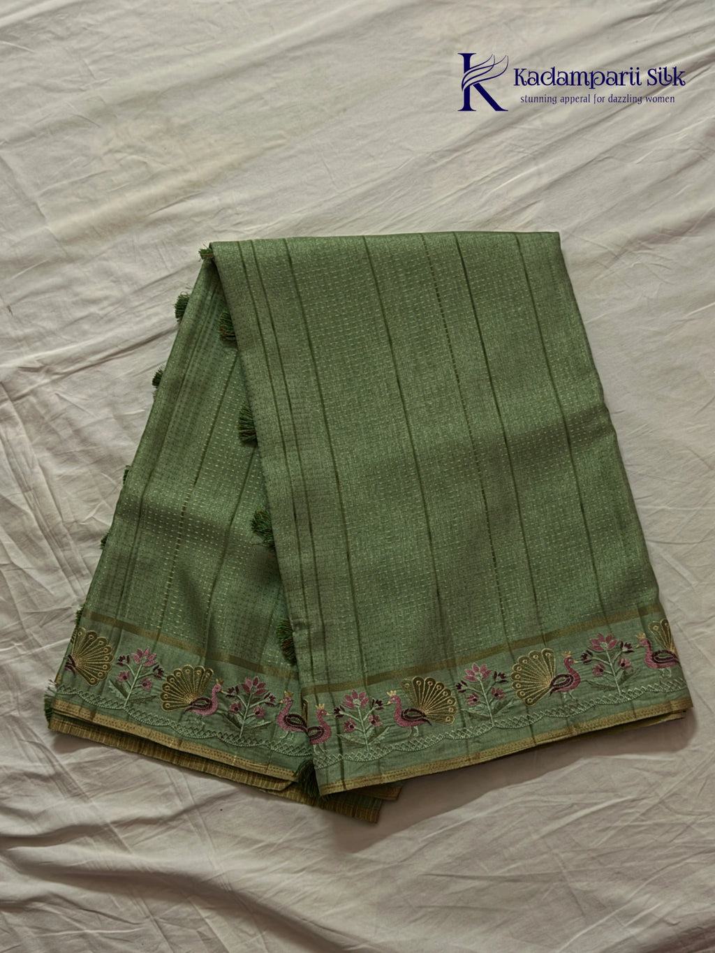 Sage green Tussar silk saree with embroidered peacock and floral border, subtle zari detailing, textured lightweight fabric, tassel finish, and elegant traditional styling by Kadamparii Silk.