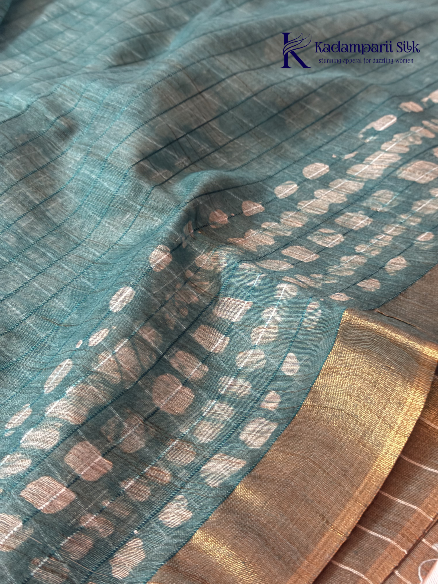 Kadamparii Silk teal semi tussar batik printed saree with abstract geometric patterns, subtle golden woven accents, soft textured fabric, tassel detailing, and elegant traditional design.