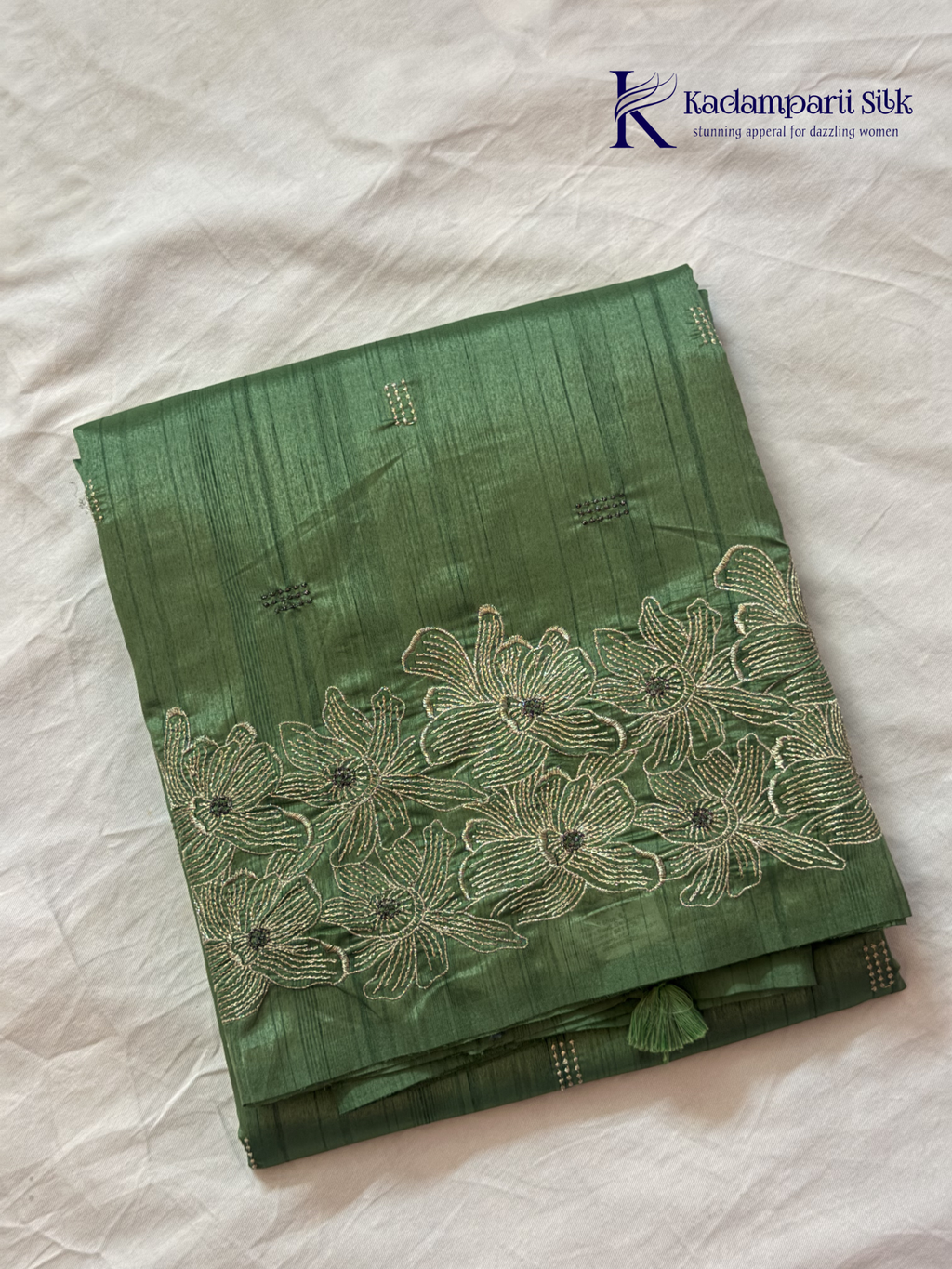 Emerald green semi raw silk saree with intricate floral embroidery, delicate embellishment detailing, rich textured finish, elegant tassels, and graceful festive drape by Kadamparii Silk.