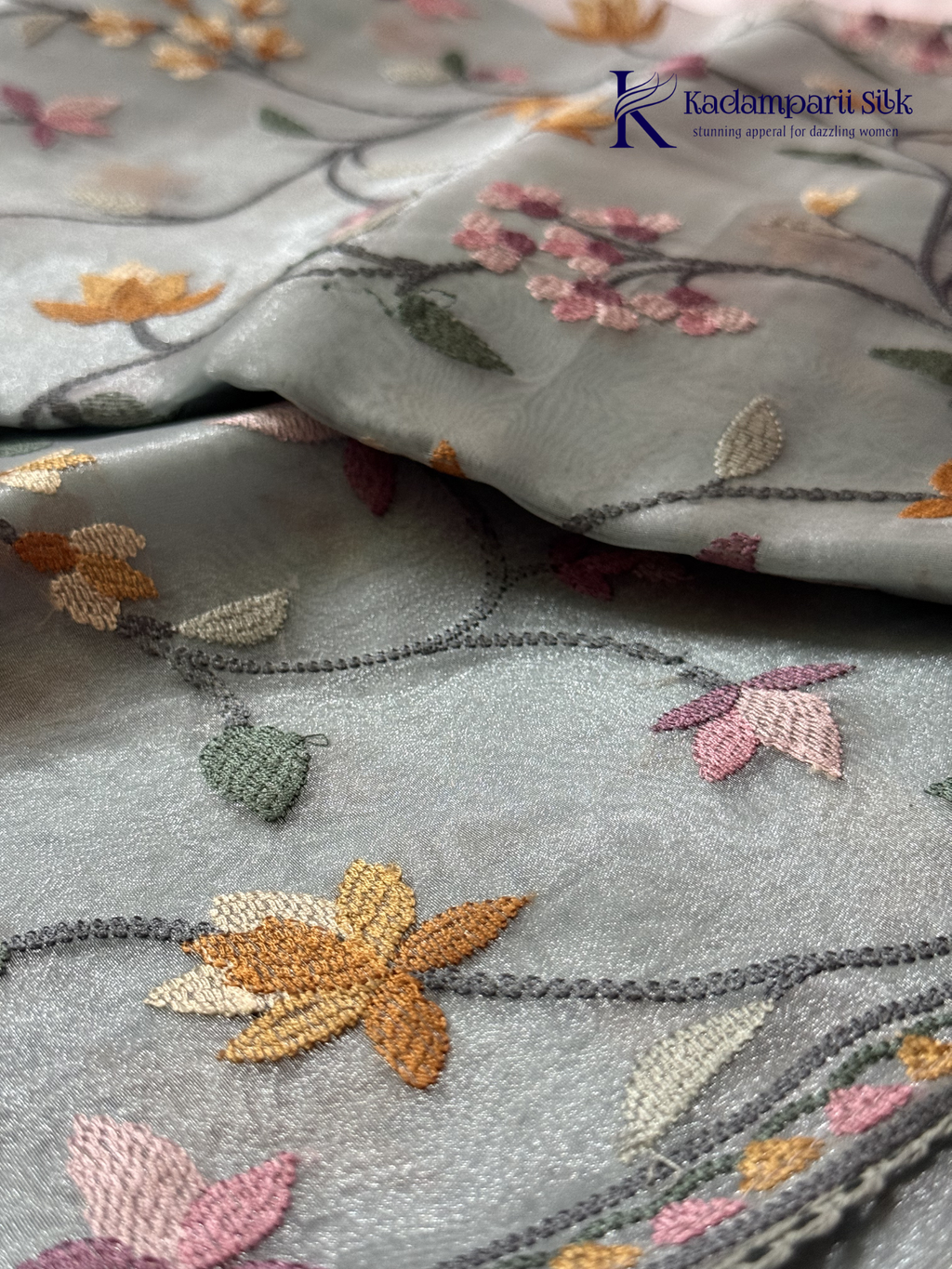 Pastel blue organza saree with multicolor floral embroidery, delicate vine patterns, embroidered border detailing, lightweight sheer fabric, and elegant festive styling by Kadamparii Silk.
