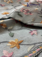 Pastel blue organza saree with multicolor floral embroidery, delicate vine patterns, embroidered border detailing, lightweight sheer fabric, and elegant festive styling by Kadamparii Silk.