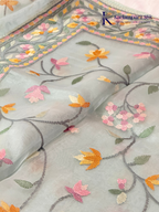 Pastel blue organza saree with multicolor floral embroidery, delicate vine patterns, embroidered border detailing, lightweight sheer fabric, and elegant festive styling by Kadamparii Silk.