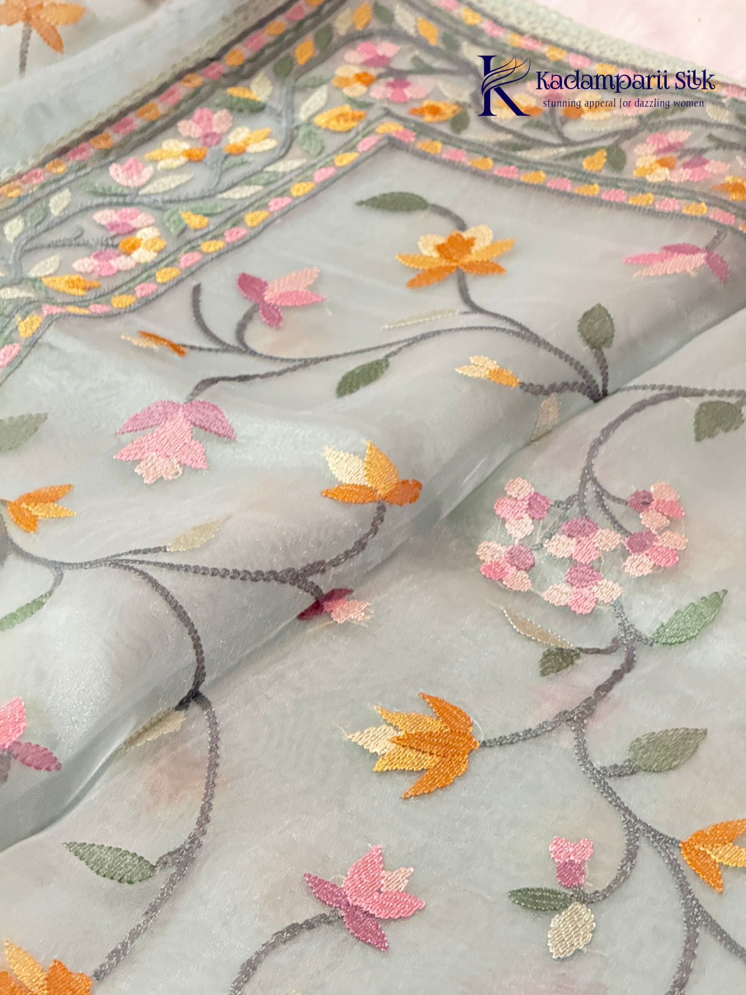 Pastel blue organza saree with multicolor floral embroidery, delicate vine patterns, embroidered border detailing, lightweight sheer fabric, and elegant festive styling by Kadamparii Silk.