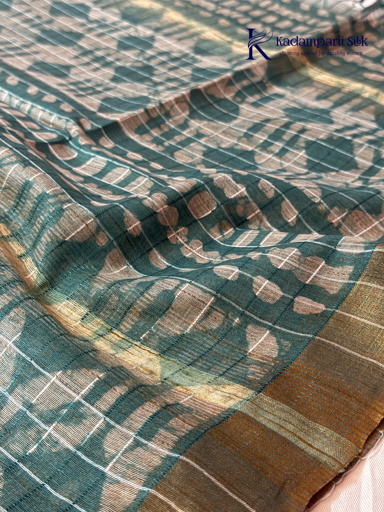 Kadamparii Silk teal semi tussar batik printed saree with abstract geometric patterns, subtle golden woven accents, soft textured fabric, tassel detailing, and elegant traditional design.