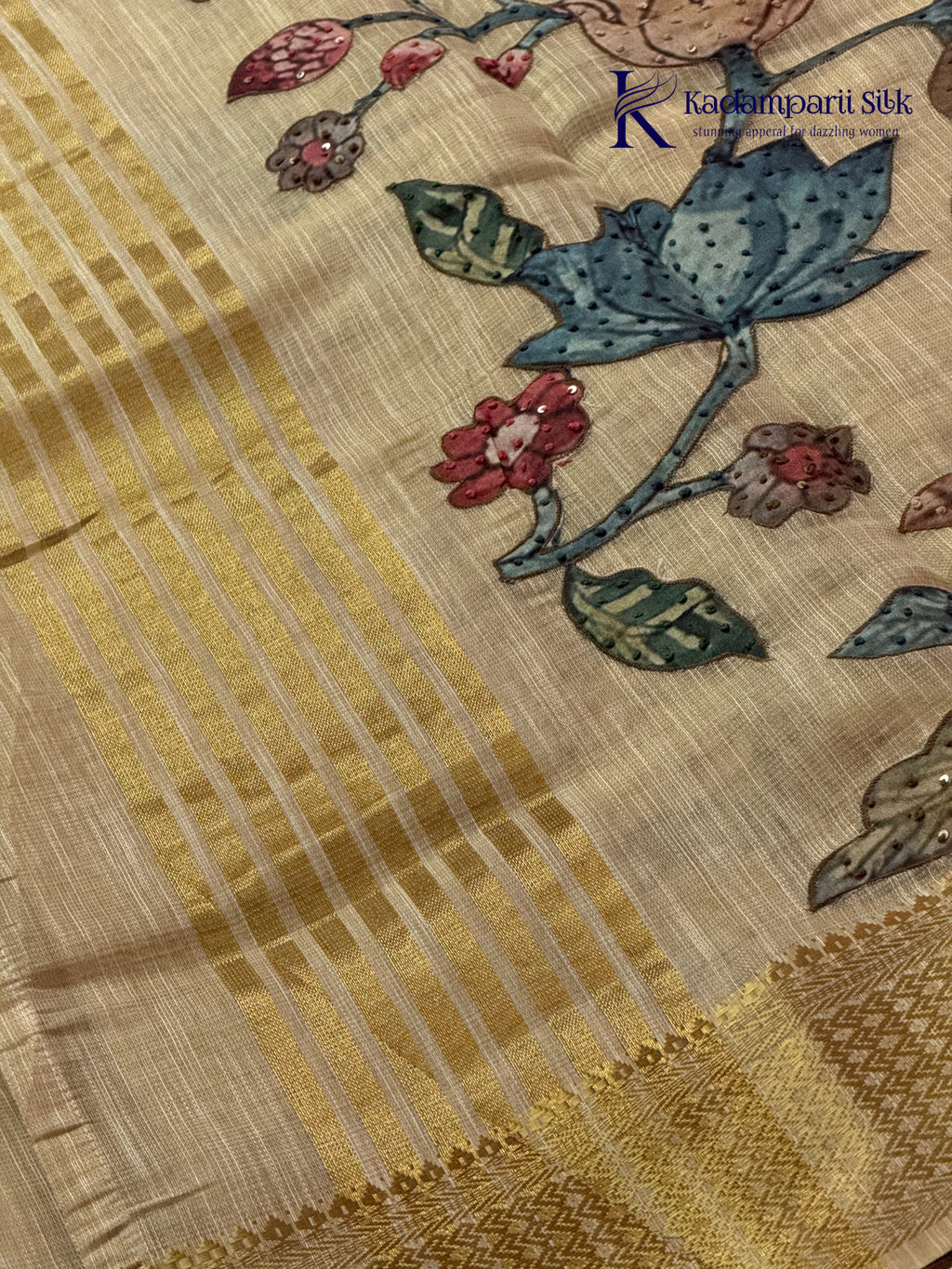 Beige silk cotton saree with colorful Kalamkari-inspired appliqué floral work, elegant woven golden border, handcrafted artistic detailing, soft texture, tassel finish, and graceful traditional drape by Kadamparii Silk.