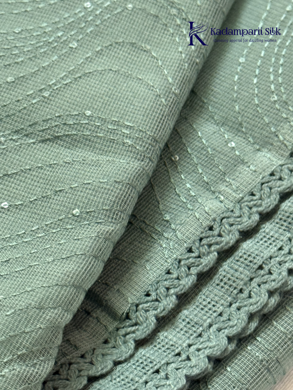 Sage green super net saree with elegant wave-pattern fancy embroidery, subtle shimmer detailing, delicate lace border, lightweight sheer texture, and graceful contemporary drape by Kadamparii Silk.
