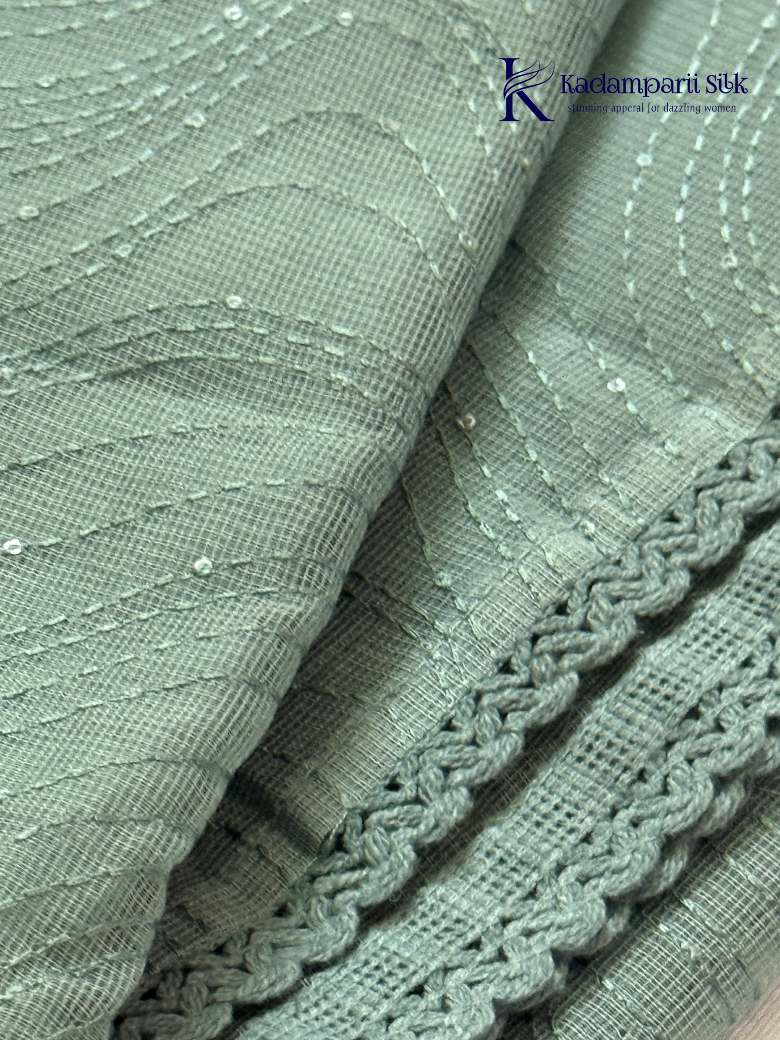 Sage green super net saree with elegant wave-pattern fancy embroidery, subtle shimmer detailing, delicate lace border, lightweight sheer texture, and graceful contemporary drape by Kadamparii Silk.