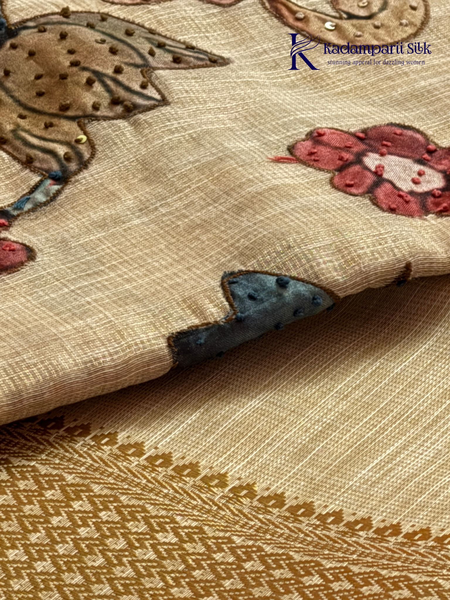 Beige silk cotton saree with colorful Kalamkari-inspired appliqué floral work, elegant woven golden border, handcrafted artistic detailing, soft texture, tassel finish, and graceful traditional drape by Kadamparii Silk.