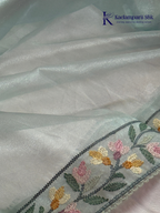 Pastel blue organza saree with multicolor floral embroidery, delicate vine patterns, embroidered border detailing, lightweight sheer fabric, and elegant festive styling by Kadamparii Silk.
