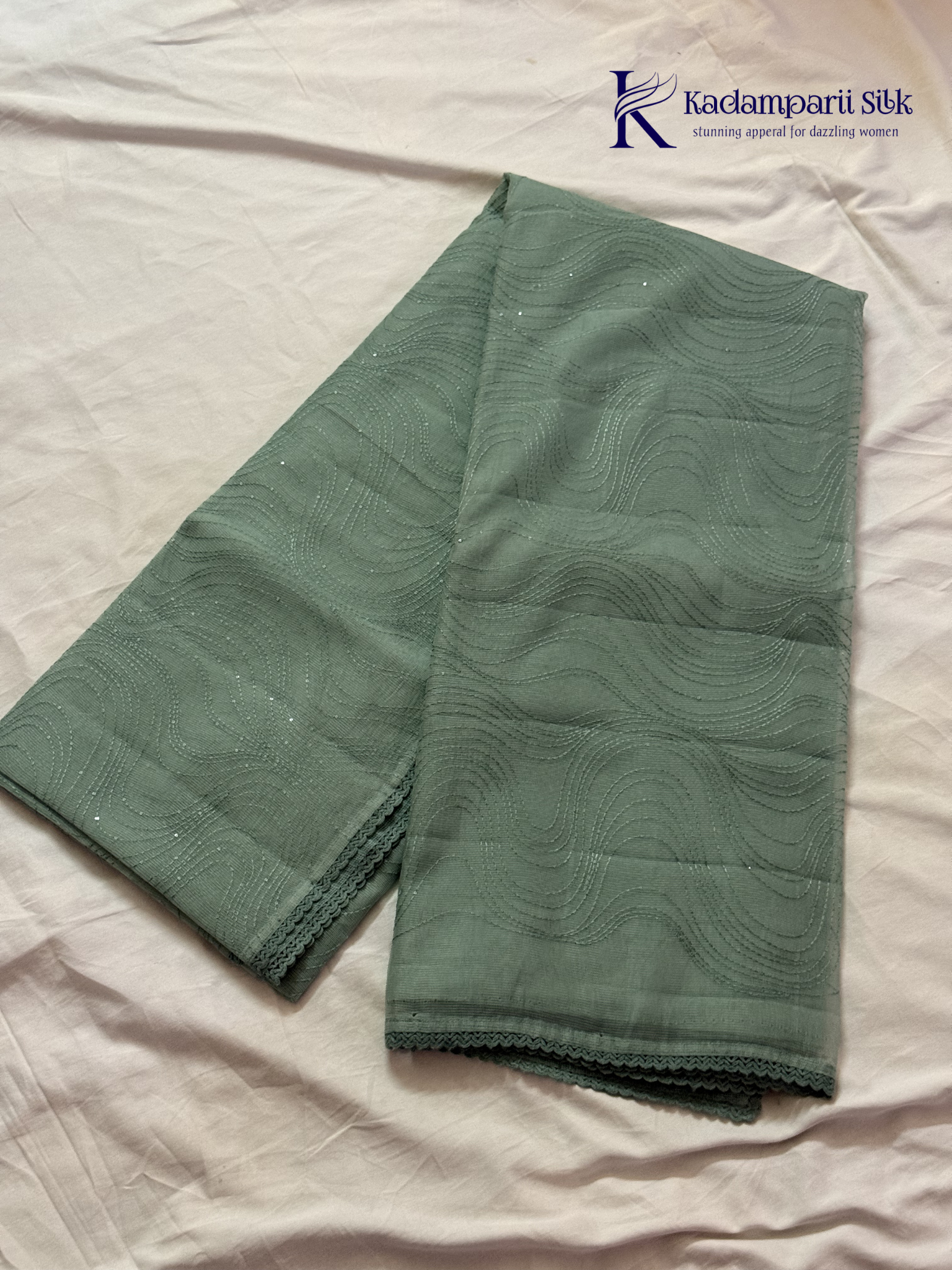 Sage green super net saree with elegant wave-pattern fancy embroidery, subtle shimmer detailing, delicate lace border, lightweight sheer texture, and graceful contemporary drape by Kadamparii Silk.