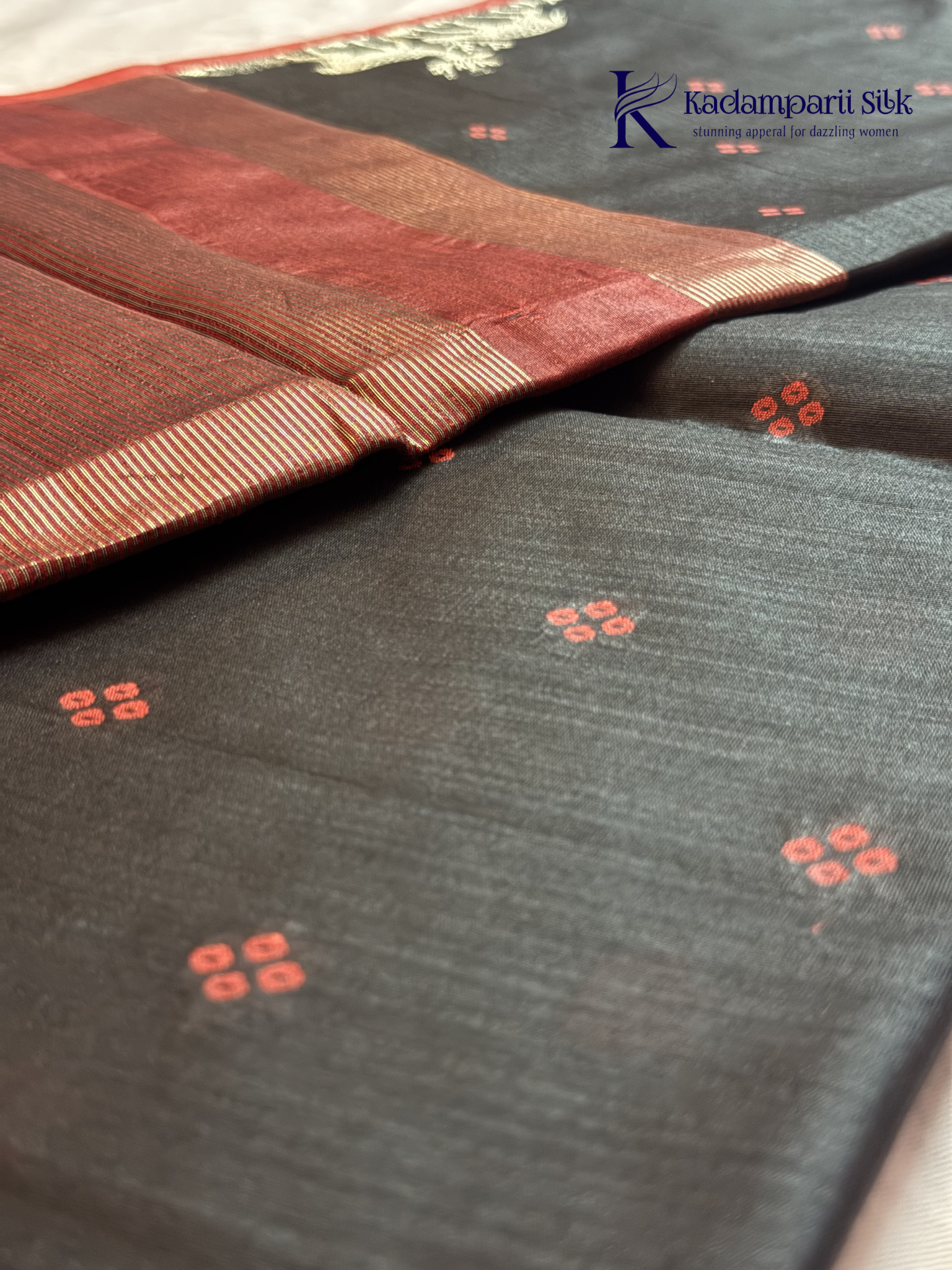 Black semi raw silk saree with red butta motifs, elegant zari woven border and pallu, soft lightweight texture, tassel detailing, and traditional ethnic styling by Kadamparii Silk.