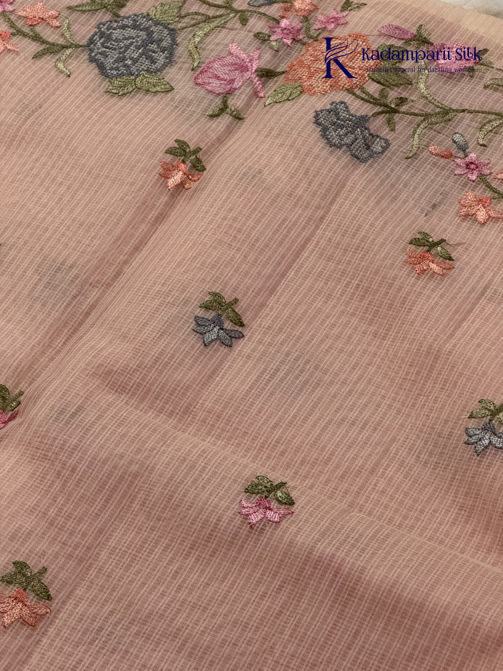 Blush pink super net saree with delicate multicolor floral embroidery, soft textured weave, lightweight sheer fabric, elegant feminine detailing, and graceful modern drape by Kadamparii Silk.