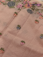 Blush pink super net saree with delicate multicolor floral embroidery, soft textured weave, lightweight sheer fabric, elegant feminine detailing, and graceful modern drape by Kadamparii Silk.