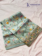 Pastel blue organza saree with multicolor floral embroidery, delicate vine patterns, embroidered border detailing, lightweight sheer fabric, and elegant festive styling by Kadamparii Silk.