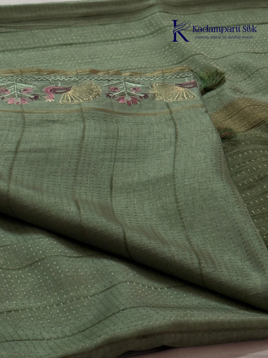 Sage green Tussar silk saree with embroidered peacock and floral border, subtle zari detailing, textured lightweight fabric, tassel finish, and elegant traditional styling by Kadamparii Silk.