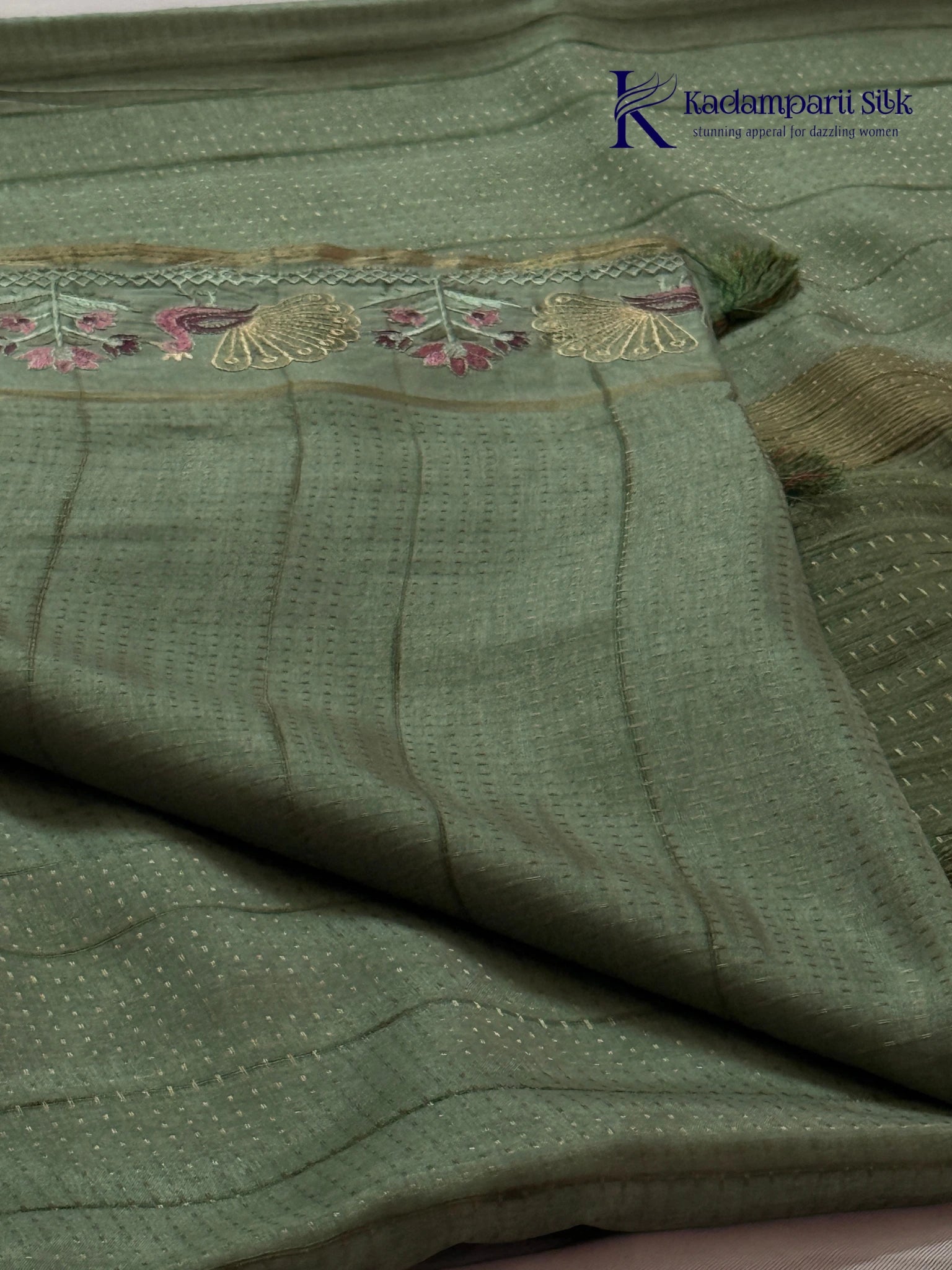 Sage green Tussar silk saree with embroidered peacock and floral border, subtle zari detailing, textured lightweight fabric, tassel finish, and elegant traditional styling by Kadamparii Silk.