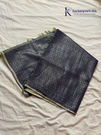 Charcoal grey semi Tussar jacquard saree with intricate woven self-patterns, subtle silver zari border, soft textured finish, elegant tassels, and lightweight graceful drape by Kadamparii Silk.