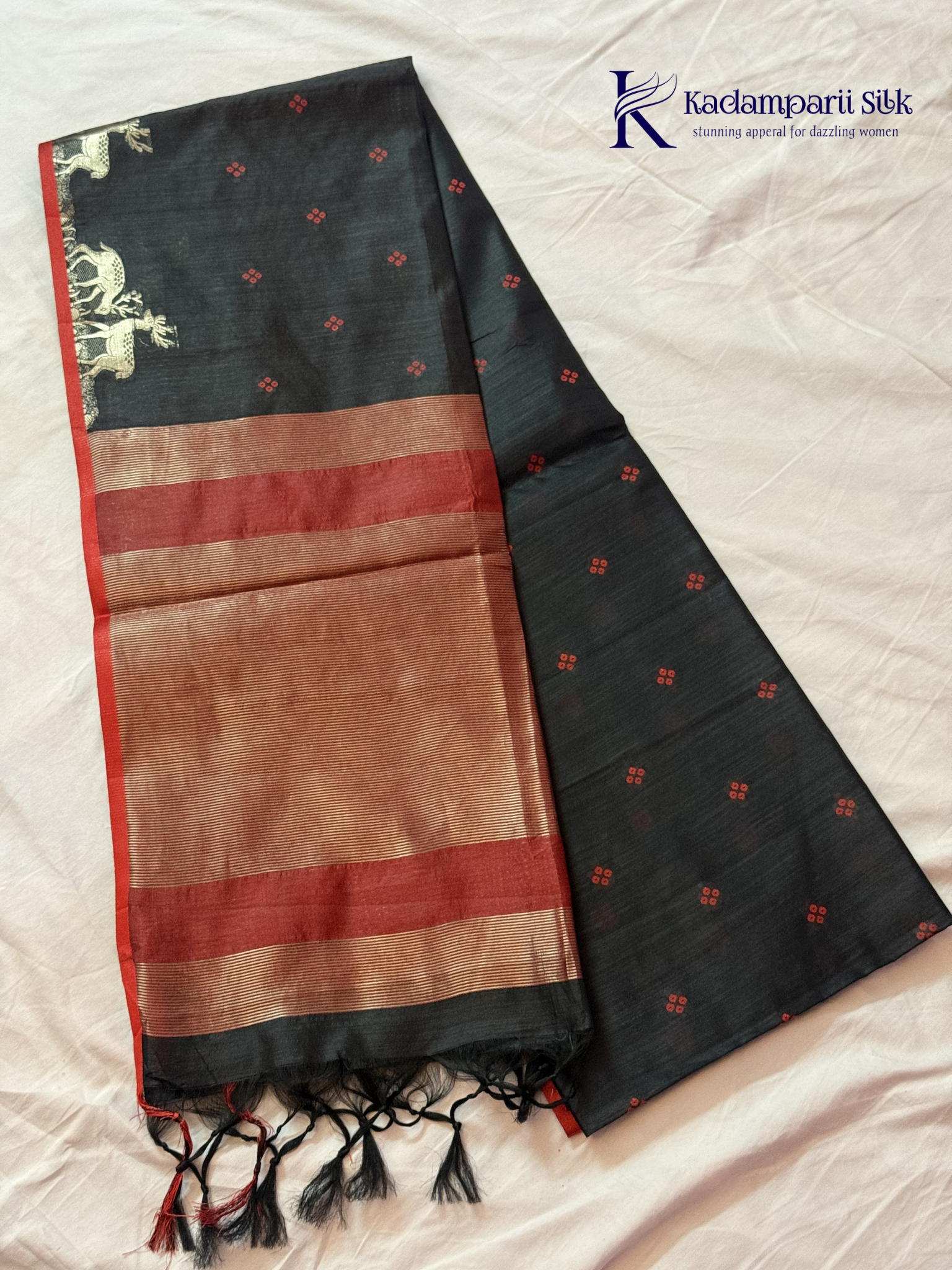 Black semi raw silk saree with red butta motifs, elegant zari woven border and pallu, soft lightweight texture, tassel detailing, and traditional ethnic styling by Kadamparii Silk.