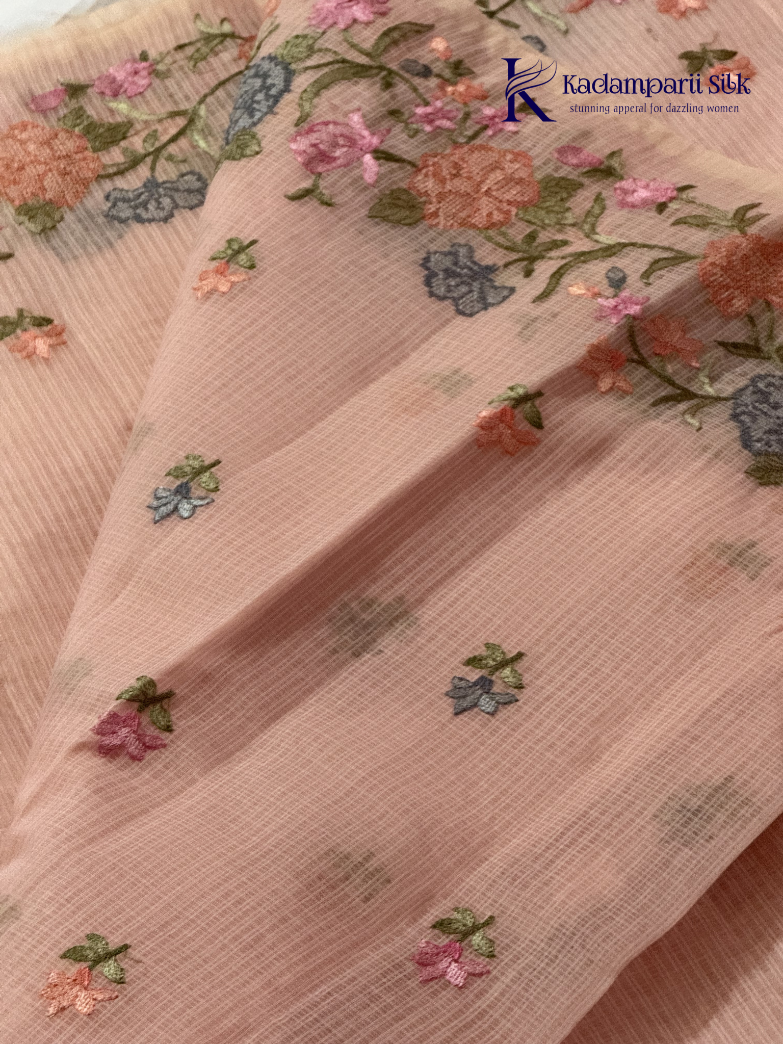 Blush pink super net saree with delicate multicolor floral embroidery, soft textured weave, lightweight sheer fabric, elegant feminine detailing, and graceful modern drape by Kadamparii Silk.