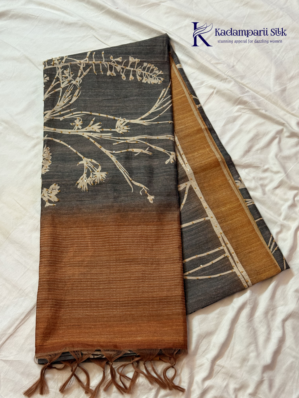 Grey Chenderi silk cotton saree with elegant floral vine design, intricate French knot work, copper-toned border and pallu, soft lightweight fabric, tassel detailing, and graceful ethnic styling by Kadamparii Silk.