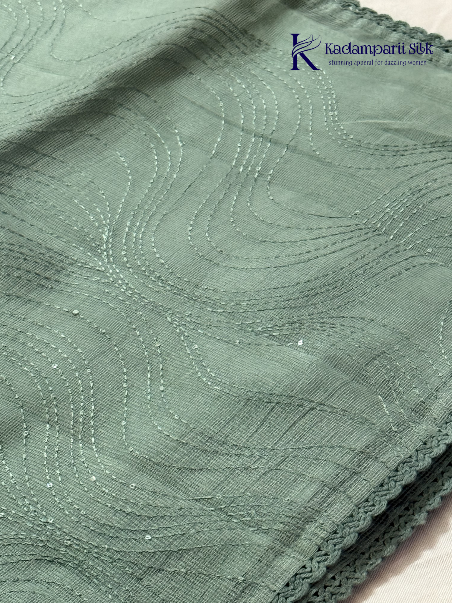 Sage green super net saree with elegant wave-pattern fancy embroidery, subtle shimmer detailing, delicate lace border, lightweight sheer texture, and graceful contemporary drape by Kadamparii Silk.
