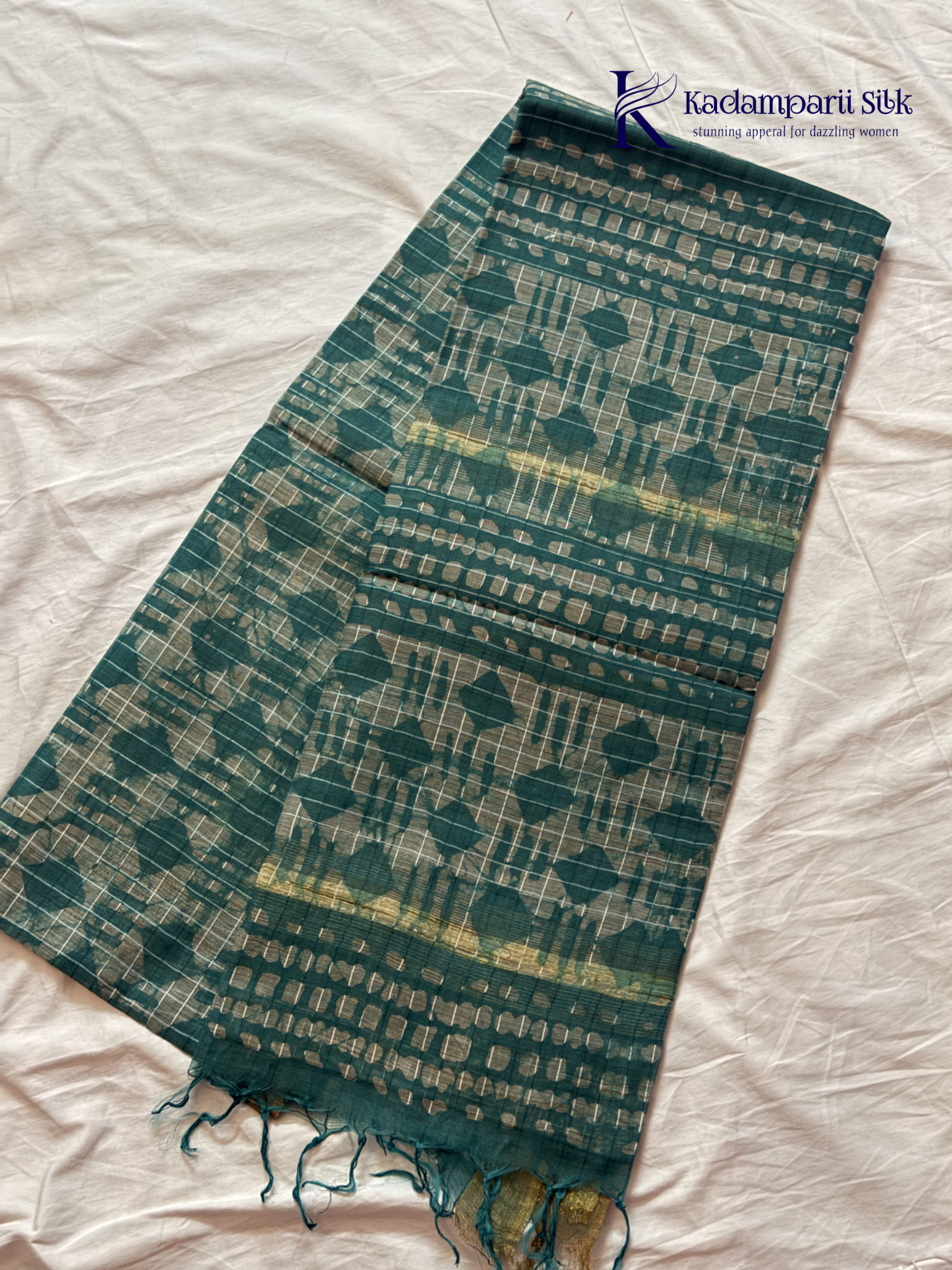 Kadamparii Silk teal semi tussar batik printed saree with abstract geometric patterns, subtle golden woven accents, soft textured fabric, tassel detailing, and elegant traditional design.