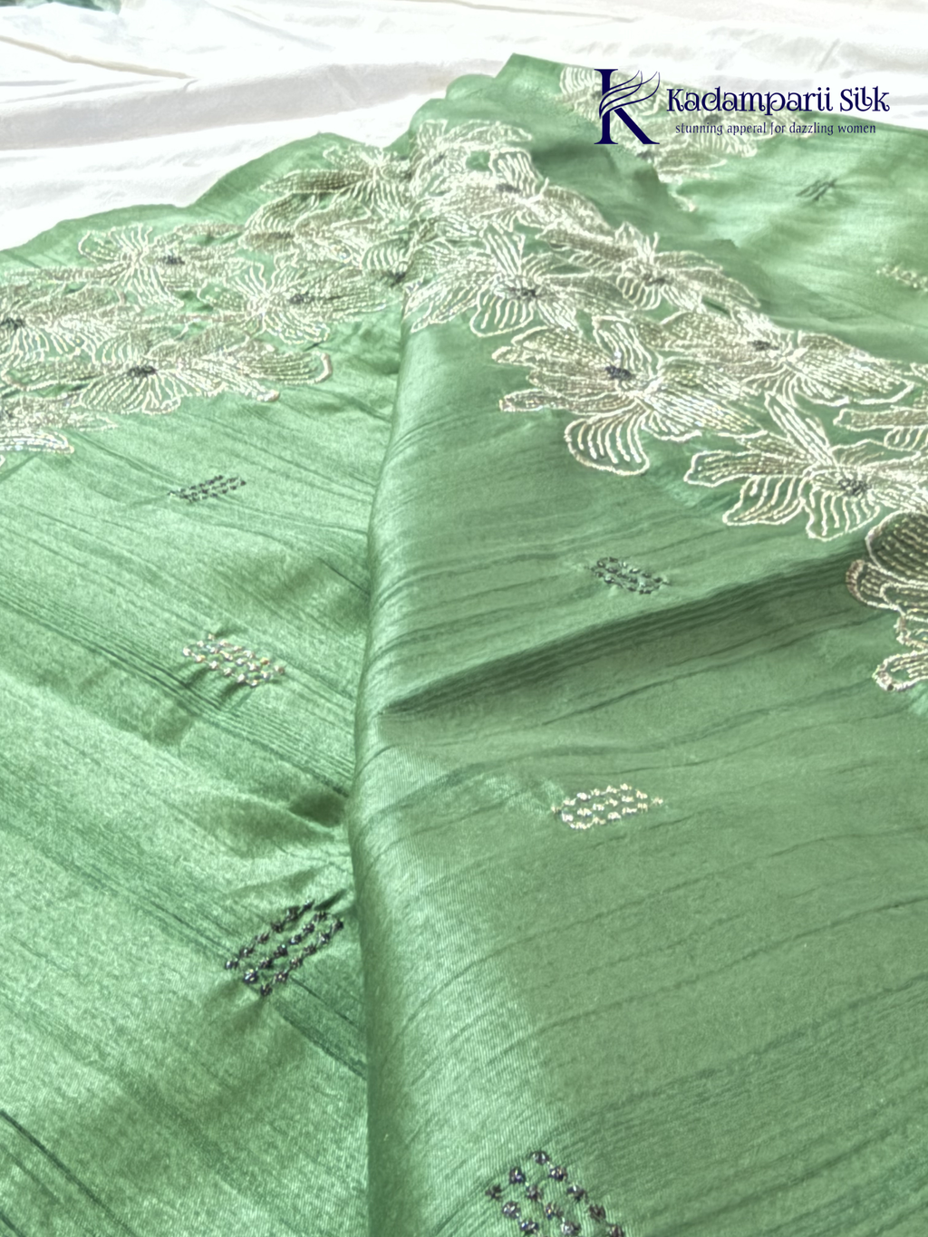 Emerald green semi raw silk saree with intricate floral embroidery, delicate embellishment detailing, rich textured finish, elegant tassels, and graceful festive drape by Kadamparii Silk.