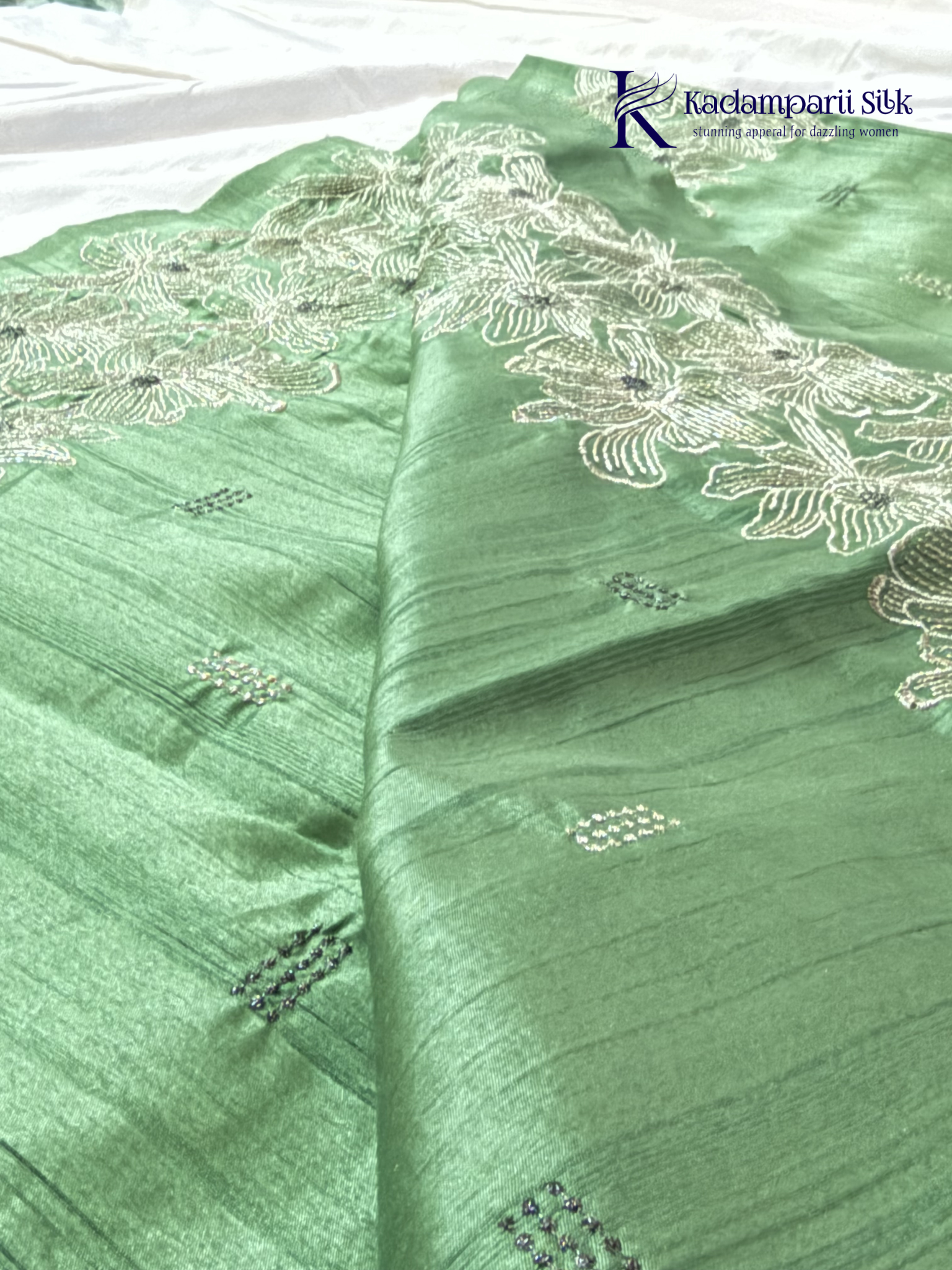 Emerald green semi raw silk saree with intricate floral embroidery, delicate embellishment detailing, rich textured finish, elegant tassels, and graceful festive drape by Kadamparii Silk.