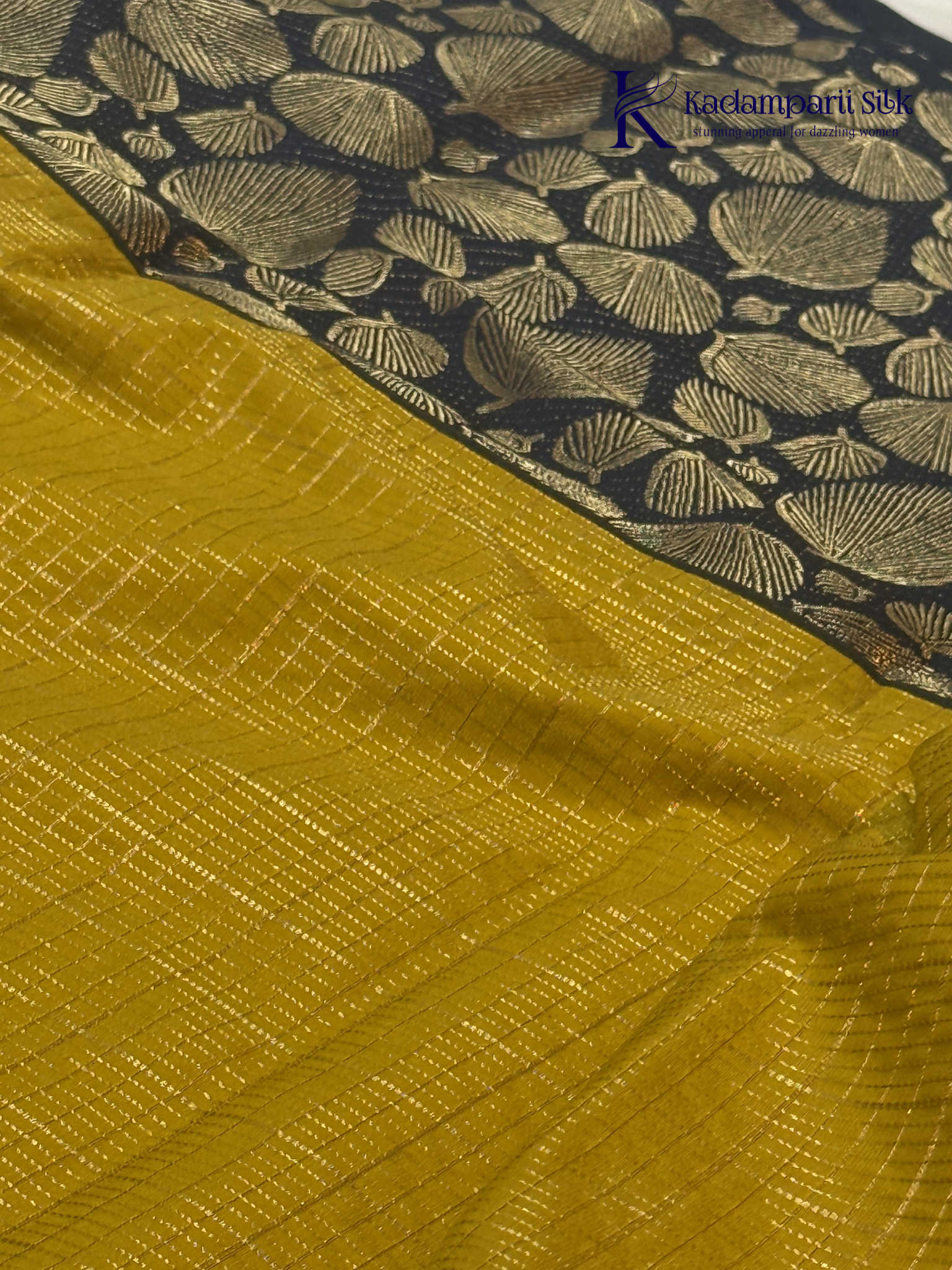 Mustard yellow art silk saree with navy blue floral zari border and textured weave displayed on white background Kadamparii SIlk