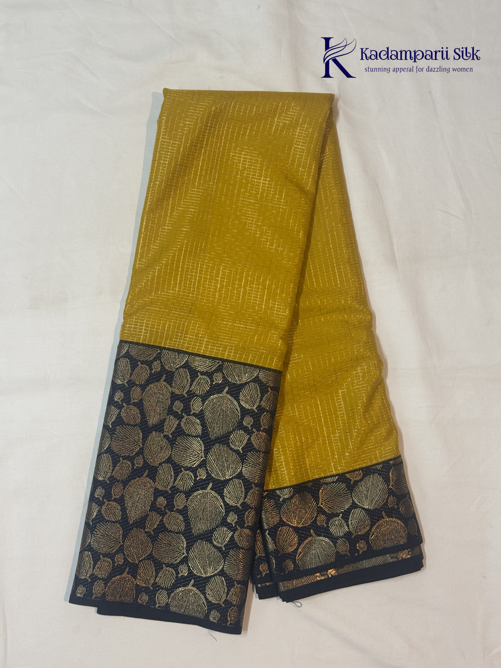 Mustard yellow art silk saree with navy blue floral zari border and textured weave displayed on white background Kadamparii SIlk