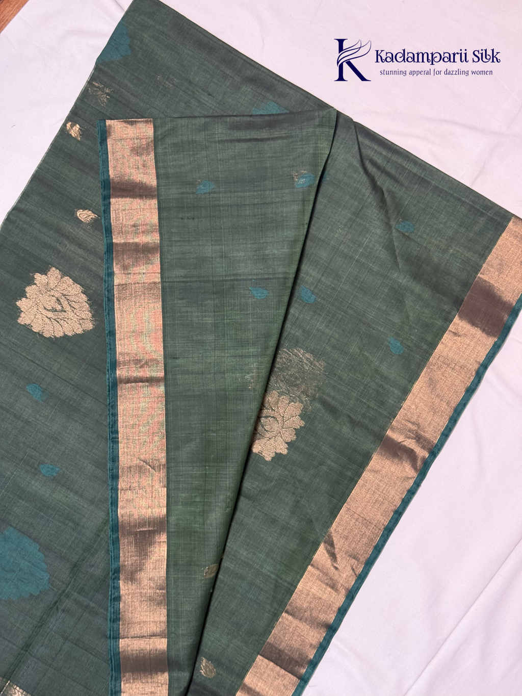 Green saree with gold and blue patterns on a white background, featuring the Kadambarii Silk brand.Silk Cotton