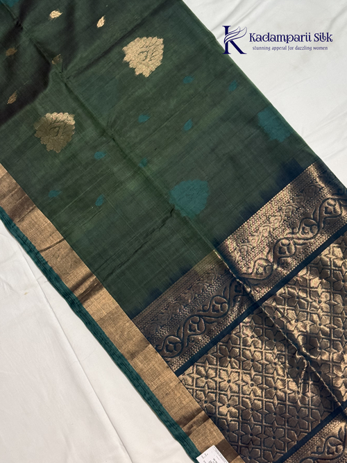 Green saree with gold and blue patterns on a white background, featuring the Kadambarii Silk brand.Silk Cotton